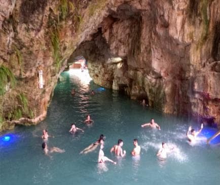 Bañistas en un cenote de agua turquesa dentro de una cueva de roca