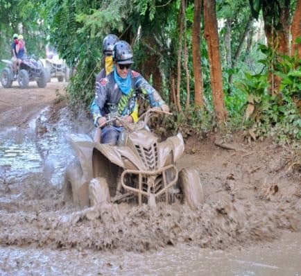 Conductor con pañuelo azul en una cuatrimoto embarrada por un sendero del bosque
