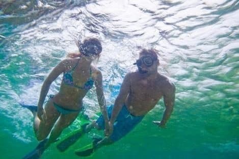 Un hombre y una mujer buceando con esnórquel y aletas bajo la superficie del agua