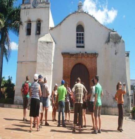 Turistas frente a una iglesia colonial blanca con campanario