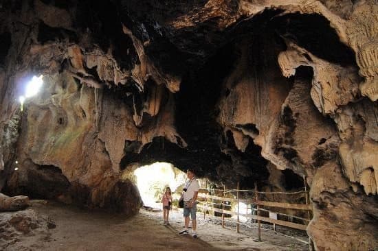 Dos visitantes en una cueva con formaciones de roca, junto a una baranda de madera