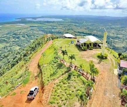 Vista aérea de la cima de una colina con edificios, palmeras y una camioneta en un camino de tierra
