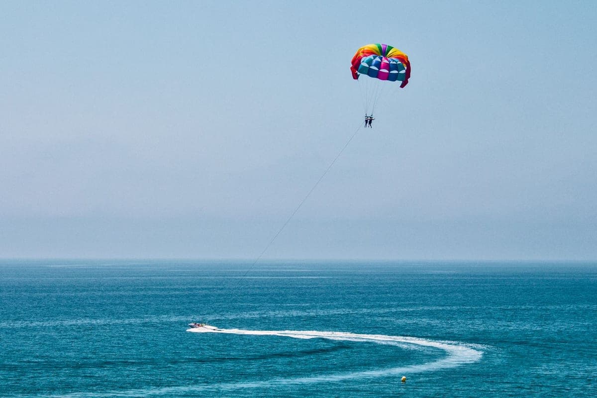 Dos personas en parasailing bajo un parapente de colores, remolcadas por una lancha sobre el mar