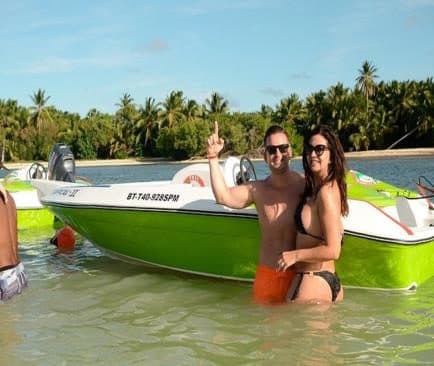 Pareja de pie en agua poco profunda junto a una lancha verde