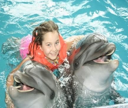 Niña con chaleco salvavidas entre dos delfines